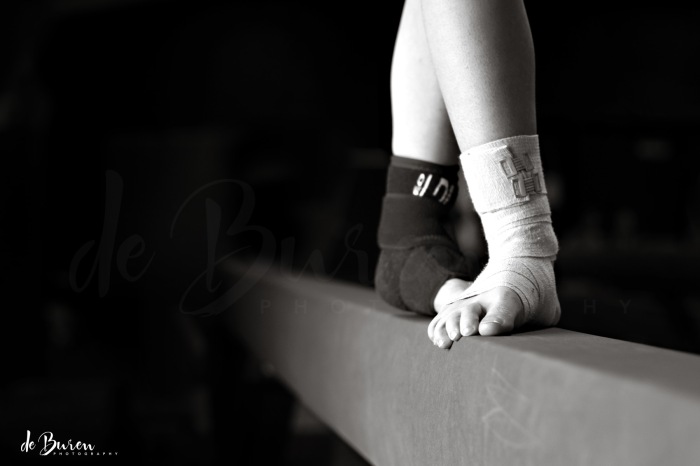 dedicated young gymnast with ankles wrapped standing on balance beam